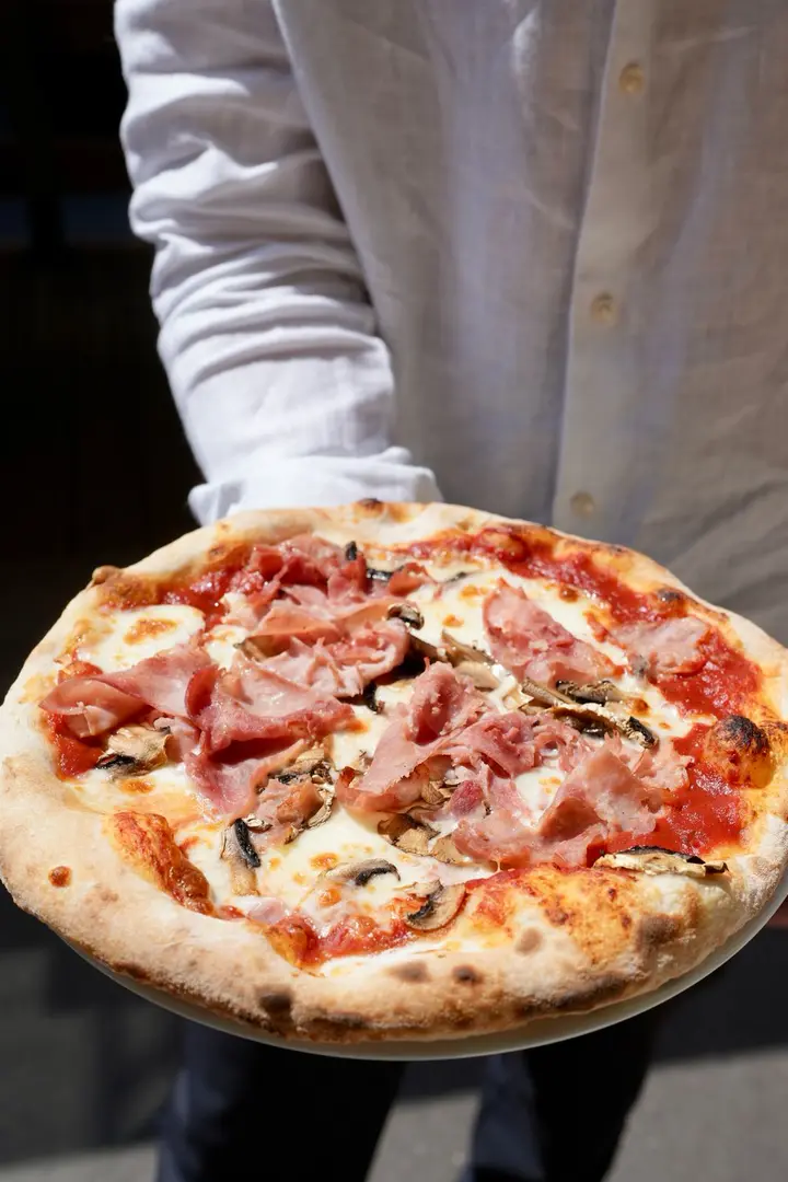 A ham and mushroom pizza held by a waiter